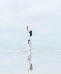 画像：海辺でロングヘアの女性が空に手を上げている様子